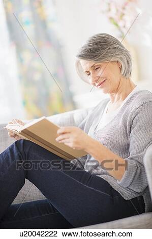 Stock Image - Portrait of woman reading on sofa. Fotosearch