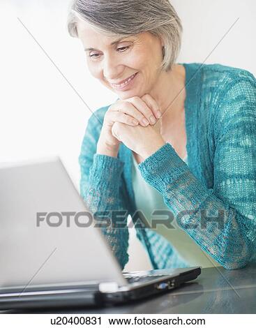 Stock Image - Portrait of woman sitting in front of laptop. Fotosearch