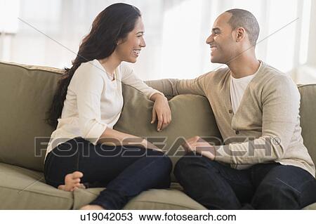 Stock Image - Portrait of young couple sitting on couch. Fotosearch