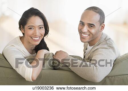 Stock Photograph - Portrait of young couple sitting on couch. Fotosearch