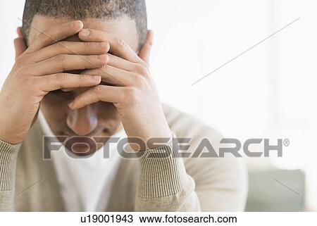 Stock Image - Portrait of young man holding head in hands. Fotosearch