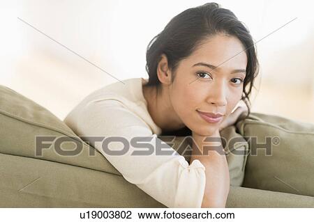 Stock Image - Portrait of young woman sitting on couch. Fotosearch