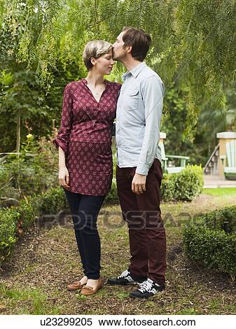 Stock Photography - Pregnant couple embracing and kissing in garden. Fotosearch