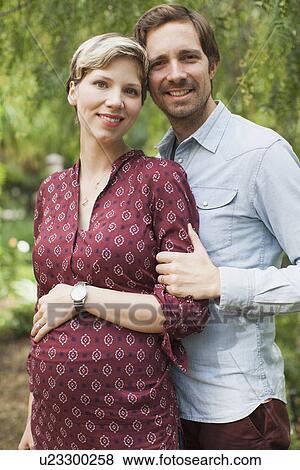 Stock Photo - Pregnant couple embracing in garden. Fotosearch