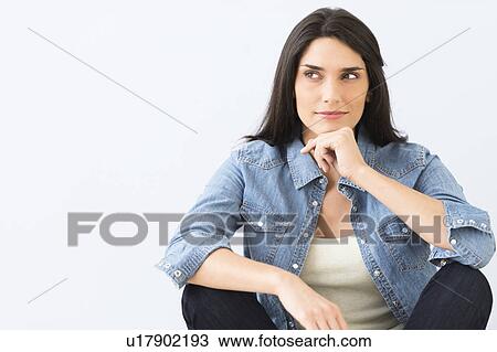 Stock Image - Studio portrait of young woman sitting on floor. Fotosearch