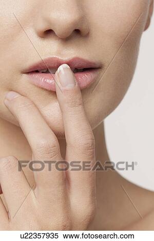 Stock Photography - Studio shot portrait of young woman in white blouse with finger on lips. Fotosearch