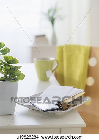 Picture - View of mug, flower pot, mobile phone, key and paper on table. Fotosearch