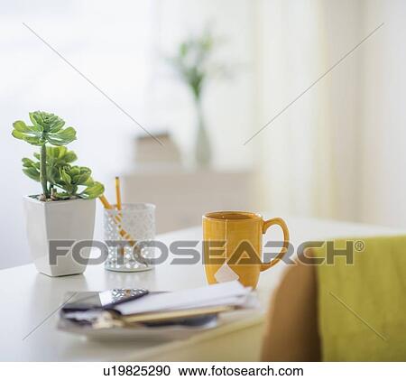 Stock Image - View of mug, flower pot, mobile phone and paper on table. Fotosearch