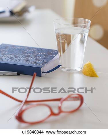 Picture - View of spectacles, personal organizer and glass of water on table. Fotosearch