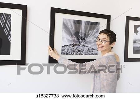 Stock Image - Woman hanging photographs in art gallery. Fotosearch