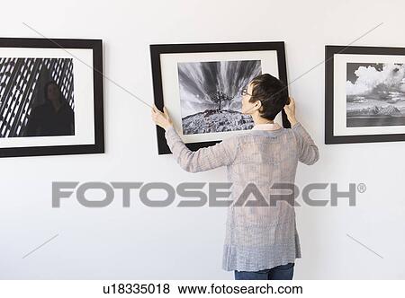 Stock Photo - Woman hanging photographs in art gallery. Fotosearch