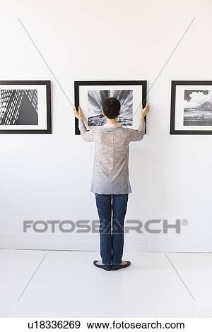 Woman hanging photographs in art gallery View Large Photo Image Stock Photo - Woman hanging photographs in art gallery. Fotosearch