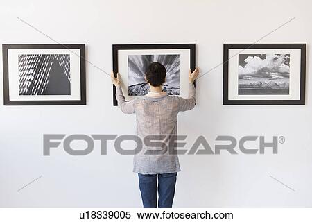 Stock Photography - Woman hanging photographs in art gallery. Fotosearch
