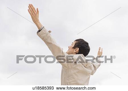 Stock Image - Woman in raincoat raising arms up into cloudy sky. Fotosearch