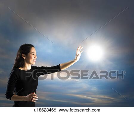 Stock Photography - Woman reaching sun on sky, studio shot. Fotosearch