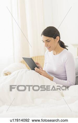 Woman sitting in bed and using digital tablet View Large Photo Image Stock Image - Woman sitting in bed and using digital tablet. Fotosearch