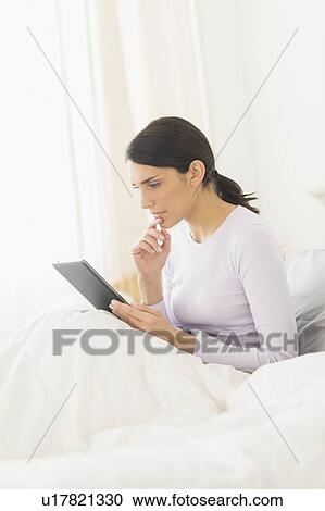 Woman sitting in bed and using digital tablet View Large Photo Image Stock Image - Woman sitting in bed and using digital tablet. Fotosearch