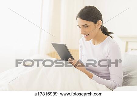 Woman sitting in bed and using digital tablet View Large Photo Image Stock Photo - Woman sitting in bed and using digital tablet. Fotosearch