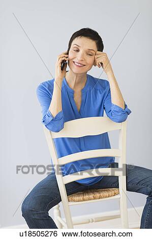 Woman sitting on chair and using mobile phone View Large Photo Image Stock Photograph - Woman sitting on chair and using mobile phone. Fotosearch