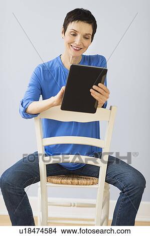 Woman sitting on chair and using digital tablet View Large Photo Image Picture - Woman sitting on chair and using digital tablet. Fotosearch
