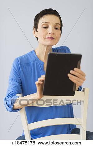 Woman sitting on chair and using digital tablet View Large Photo Image Stock Photo - Woman sitting on chair and using digital tablet. Fotosearch