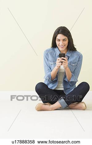 Stock Photo - Woman sitting on floor and using cell phone. Fotosearch