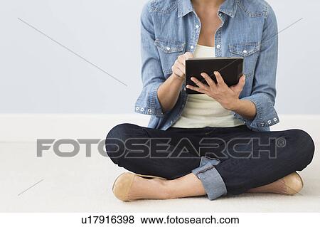 Stock Photo - Woman sitting on floor and using digital tablet. Fotosearch