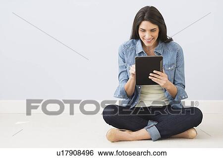 Stock Photograph - Woman sitting on floor and using digital tablet. Fotosearch