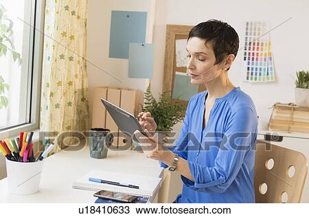 Stock Image - Woman using digital tablet in home office. Fotosearch