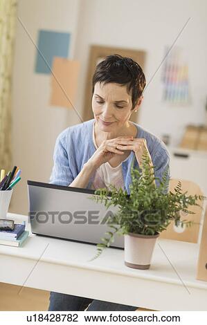 Stock Image - Woman using laptop in home office. Fotosearch