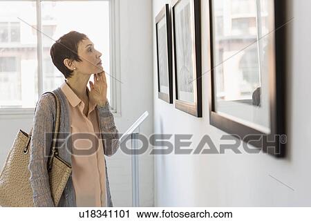 Stock Image - Woman watching photographs in art gallery. Fotosearch