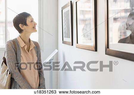 Stock Image - Woman watching photographs in art gallery. Fotosearch