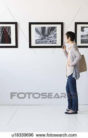 Stock Photograph - Woman watching photographs in art gallery. Fotosearch
