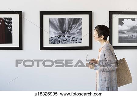 Stock Photography - Woman watching photographs in art gallery. Fotosearch
