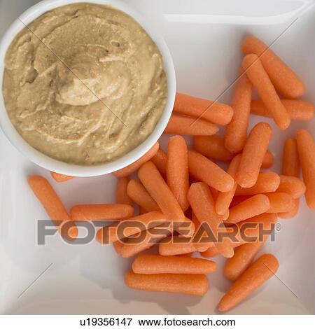 Stock Photo - Young carrots and hummus in bowl. Fotosearch