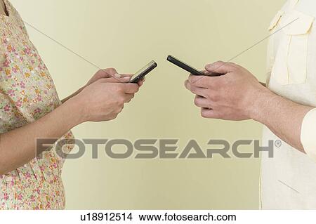 Young couple sending text messages simultaneously View Large Photo Image Picture - Young couple sending text messages simultaneously. Fotosearch