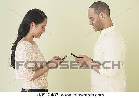 Young couple sending text messages simultaneously View Large Photo Image Stock Photo - Young couple sending text messages simultaneously. Fotosearch