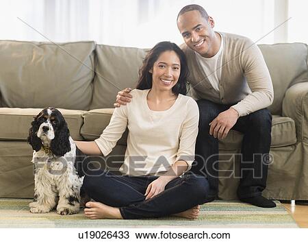 Stock Image - Young couple with dog in living room. Fotosearch