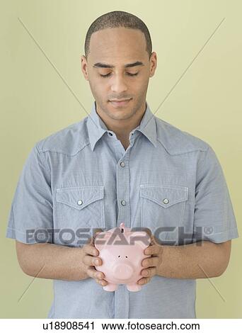 Stock Image - Young man holding piggy bank. Fotosearch