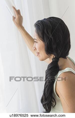 Stock Photography - Young woman looking through window. Fotosearch
