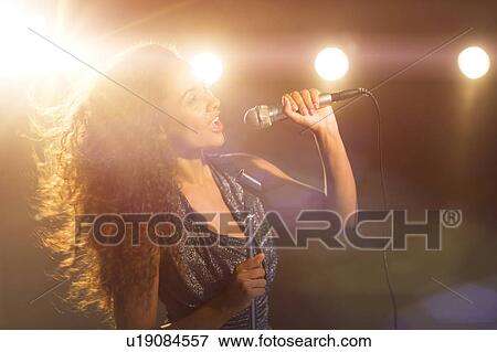 Stock Photo - Young woman singing in spotlight. Fotosearch
