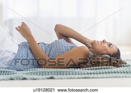 Stock Image - Young woman using phone lying on floor. Fotosearch