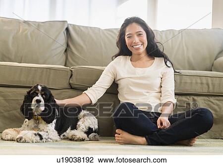 Stock Image - Young woman with dog in livingroom. Fotosearch