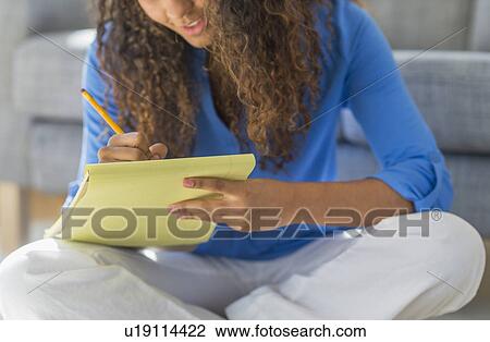 Stock Image - Young woman writing in yellow notepad. Fotosearch
