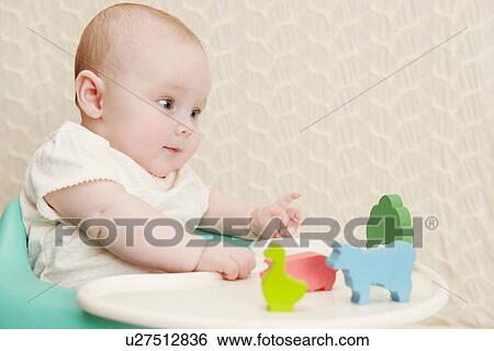 Stock Photograph - Baby girl in high chair with animal toys. Fotosearch