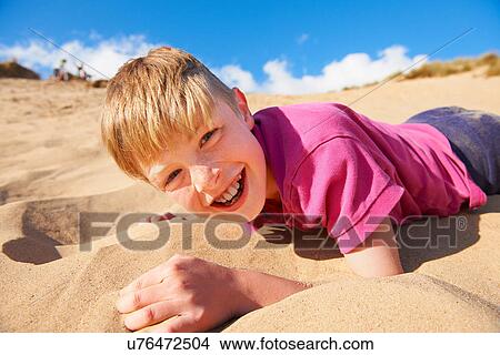 Picture - Blonde haired boy lying on beach. Fotosearch