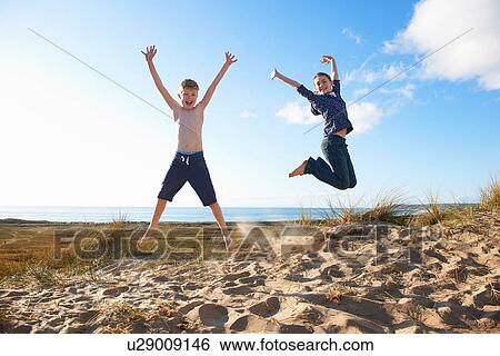 Stock Photograph - Boy and teenage girl jumping on beach. Fotosearch