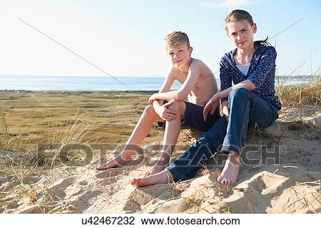 Stock Image - Boy and teenage girl sitting on beach. Fotosearch