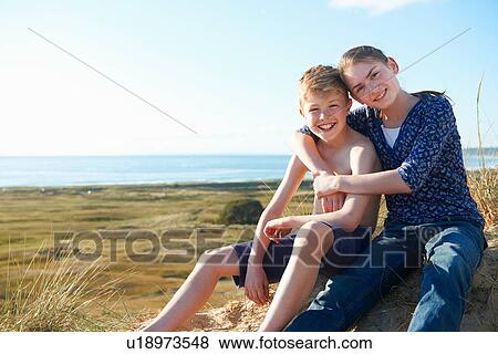 Stock Photo - Boy and teenage girl sitting on beach. Fotosearch