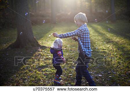 Boy blowing bubbles in forest for toddler girl View Large Photo Image Stock Photo - Boy blowing bubbles in forest for toddler girl. Fotosearch